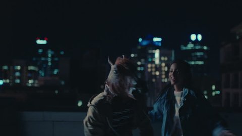 funny man wearing horse mask dancing with friends on rooftop having fun performing silly dance moves celebrating weekend together in urban city skyline