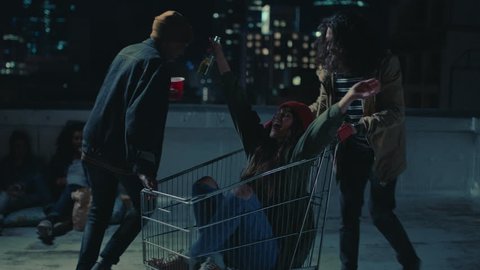 happy group of friends playing with shopping cart having fun on rooftop at night enjoying weekend celebration party