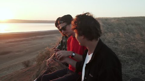 Friends skateboarders smoking weed at seashore at sunset rapid slow motion