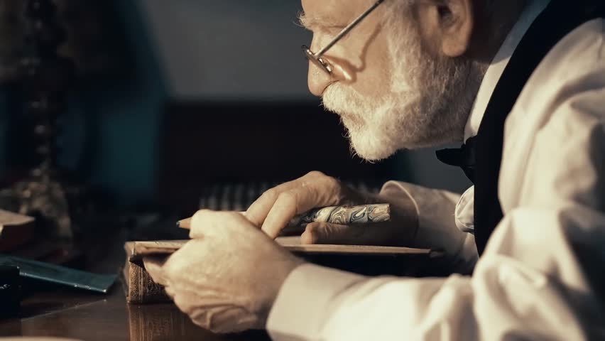 An old singer works in his creative studio, a textured writer in stylish retro clothes, a gray-haired bearded man, leafs through a notebook, writes poems and a book on a typewriter