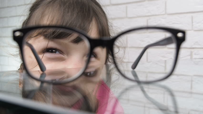 Looking through glasses. Funny girl looking through glasses lying on table. Smart child.