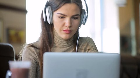 Young woman blogger working by laptop in cafe wearing headphones