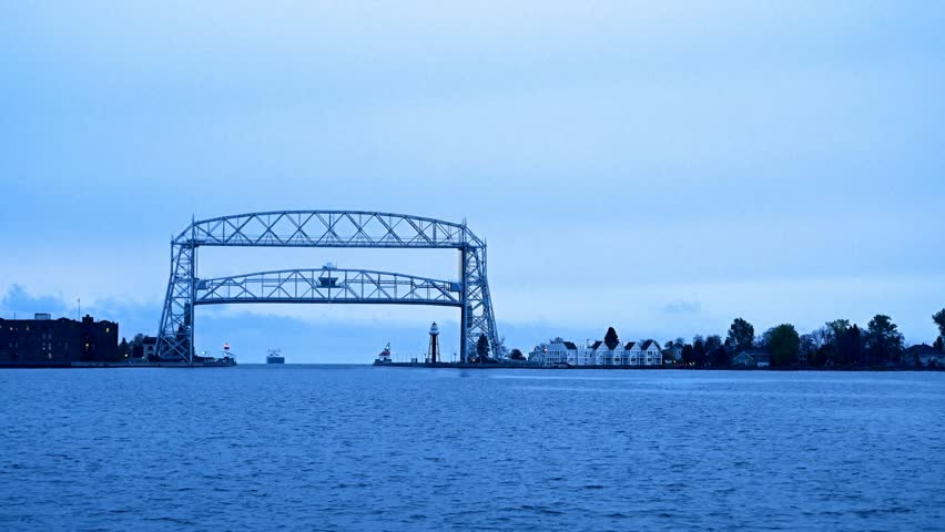 Duluth Minnesota aerial lift bridge raises as iron oar ship approaches from Lake Superior on cloudy morning