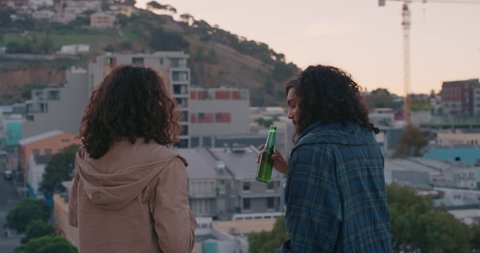 happy friends chatting on rooftop enjoying friendship reunion hanging out drinking refreshing beer sharing view of city skyline at sunset