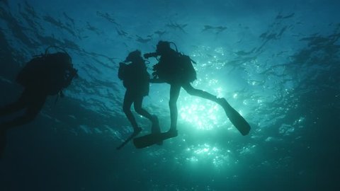 silhouette of scuba divers on surface of water underwater ascend descend sun beams and rays ocean scenery