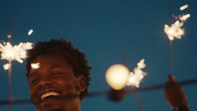 young african american man holding sparklers dancing celebrating new years eve on rooftop at night having fun with friends enjoying holiday party celebration - Powered by Shutterstock - Get 15% off with code: PIKWIZARD15