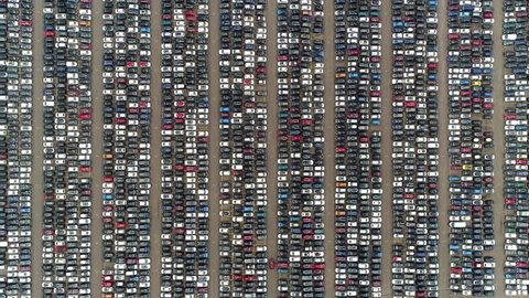Aerial top down view of automaker car distribution lot with vehicles parked close to each other in straight lines waiting for further transportation to resellers and dealers 4k high resolution footage