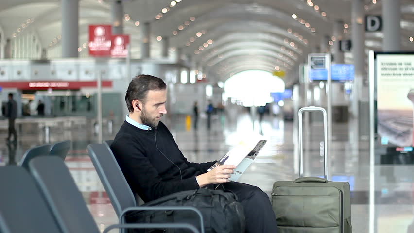 Passenger is looking at a magazine waiting at departure lounge at the airport | Shutterstock HD Video #1020259108