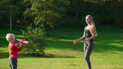 Slowmotion shot of a young woman and her little son play with an airplane on a lawn