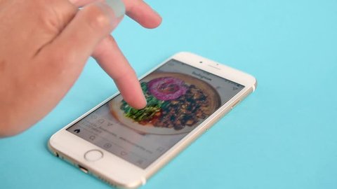 Belgrade, Serbia - November, 2018: Video of Apple Iphone 6s, showing the user scrolling Instagram feed and liking food photos, on light blue pastel background. Girls hand with grey nail color.