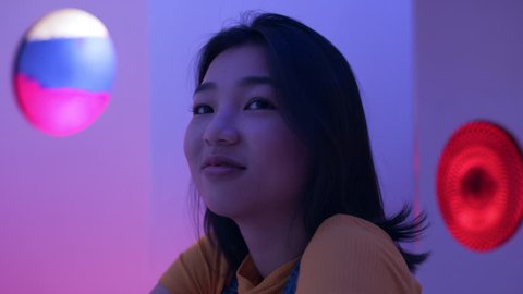 Cool Japanese woman sitting at a bar looking at the camera in a fun bar with soft interior lighting. Medium shot on 4k RED camera on a gimbal. 