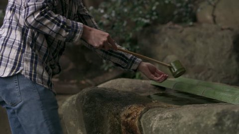 Japanese man taking water from a stone water basin and pouring it onto her hands in a beautiful garden with soft natural lighting. Medium shot on 4k RED camera.