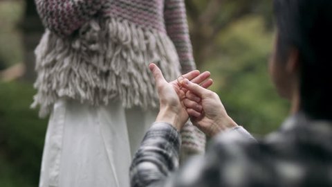 Joyful Japanese woman accepting a marriage proposal from her boyfriend and hugging him in a beautiful garden in the rain with soft natural lighting. Close up shot on 4k RED camera.