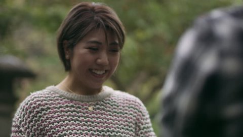 Surprised Japanese woman sees her boyfriend proposing to her with a ring and accepts happily and hugs him in a beautiful garden in the rain with soft natural lighting. Close up shot on 4k RED camera.