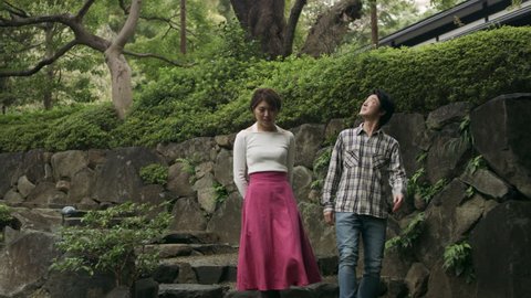 Romantic Japanese couple walking together down stone steps through a beautiful garden with soft natural lighting. Wide to Medium shot on 4k RED camera.