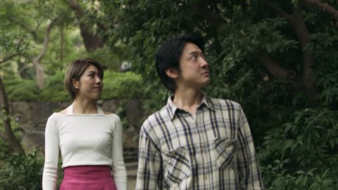 Happy Japanese couple walking together looking at the trees and plants in a beautiful garden with soft natural lighting. Wide shot on 4k RED camera.