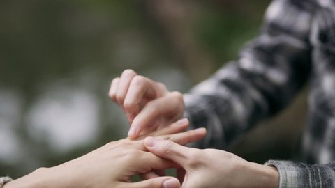 Overjoyed Japanese man presenting a ring to his girlfriend, places it on her finger and hugs her happily in a beautiful garden with soft natural lighting. Close up shot on 4k RED camera.
