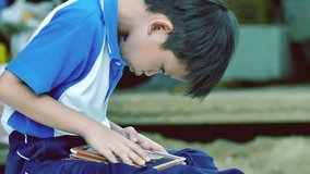 Young Asian boy playing video game on the tablet after school at home in the garden on a bright afternoon