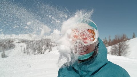 SLOW MOTION TIME WARP, CLOSE UP: Excited girl wearing ski goggles gets hit in the head by snowball. Someone trows a ball of fresh powder snow at a smiling young woman on active winter holiday.