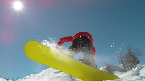 SLOW MOTION WARP, LENS FLARE, CLOSE UP Young pro snowboarder jumps off kicker and does a spinning trick. Spectacular shot of winter athlete riding his snowboard and doing a grab high in the sunny sky