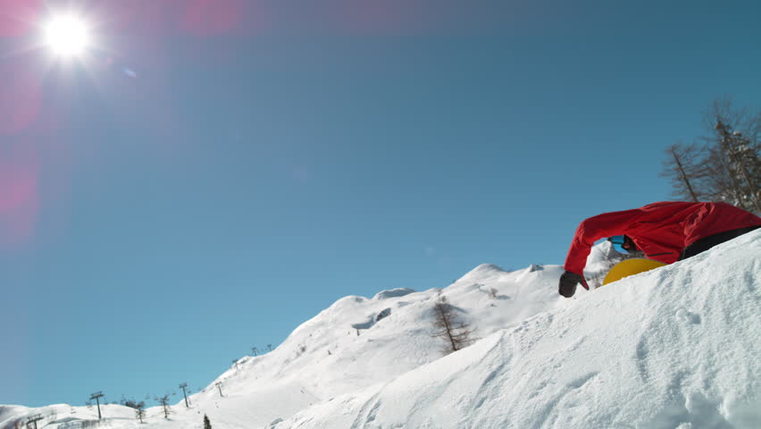 SLOW MOTION TIME REMAP, CLOSE UP, LENS FLARE: Bright winter sun shines on male snowboarder doing a pro spinning grab. Extreme man jumps off kicker and does a cool trick while riding in ski resort. Royalty-Free Stock Footage #1020268639
