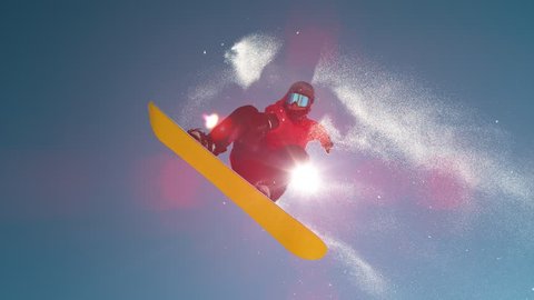 SLOW MOTION TIME REMAP, CLOSE UP, LENS FLARE: Bright winter sun shines on male snowboarder doing a pro spinning grab. Extreme man jumps off kicker and does a cool trick while riding in ski resort.