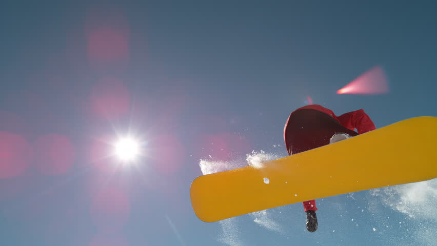 SLOW MOTION CLOSE UP: Snowboarder jumping big air kicker, spraying snowflakes and flying over sun on perfect winter day. Snowboard jump in snow park. Sunbeams shining past jumping boarder in mountains | Shutterstock HD Video #1020268642