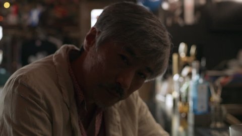 Tired, drunk Japanese man sitting at the bar counter with a cocktail in a cool bar with soft day lighting. Medium shot on 4k RED camera.