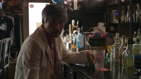 Portrait of sad, tired, drunk Japanese man sitting at the bar counter with an empty glass in a bar with soft day lighting. Medium shot on 4k RED camera.