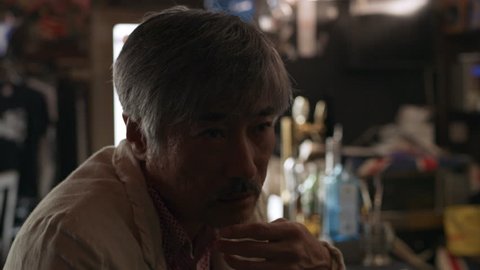 Drunk Japanese man sitting at the bar counter with a beer in a dank bar with soft day lighting. Medium shot on 4k RED camera.