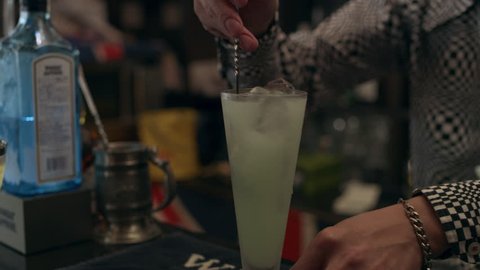 Fun Japanese bartender creating a cocktail for a customer in a cool bar with soft interior lighting. Medium shot on 4k RED camera.
