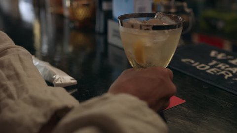 Drunk old Japanese man drinking a cocktail and thanking the bartender in a cool bar with soft natural lighting. Medium shot on 4k RED camera.