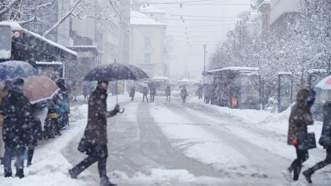 SLOVENIA, LJUBLJANA - January 2018: Snow blizzard city center in slow motion HD. Static long shot with far away vehicles in focus while people crossing the street out of focus.