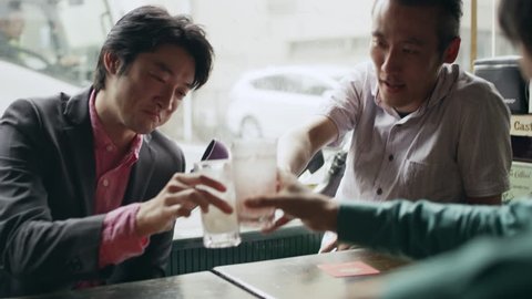 Japanese friends sitting at a table with their drinks talking happily and having fun in a cool bar with soft natural lighting. Medium shot on 4k RED camera.
