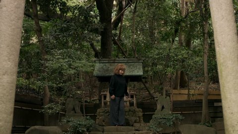Melancholic elderly woman
 walking up to a shrine and bowing towards it in a beautiful garden with soft natural lighting. Wide shot on 4k RED camera.