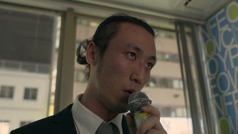 Somber, drunk Japanese man standing alone in a karaoke room and singing a song with a microphone with soft interior lighting. Close up shot on 4k RED camera.