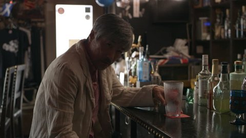 Tired, drunk Japanese man sitting at the bar counter with a cocktail in a cool bar with soft day lighting. Medium shot on 4k RED camera.