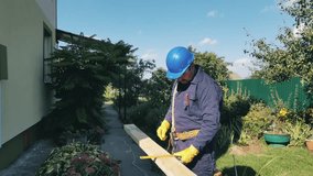 Man in gloves and blue helmet makes markings on wooden beam outdoors. Clear confident movements professional carpenter makes marks on board with pencil and carpenters square, manual labor stock video