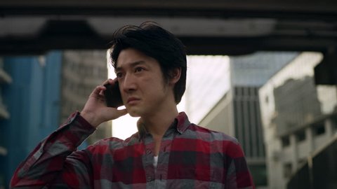 Serious and pensive Japanese man walking down a quiet metropolitan street in Japan and answers his phone with concern with soft natural lighting. Medium shot on 4k RED camera on a gimbal. 