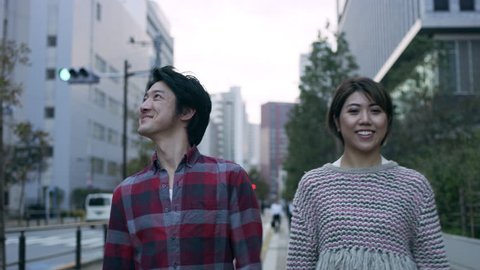 Smiling Japanese couple walking down a quiet metropolitan street with soft natural lighting. Medium shot on 4k RED camera.