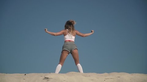 Sexy girl dancing twerk at the beach Tanned woman in short shorts moves her body standing on the sand Female is twerking outdoors Pretty lady dances passionately