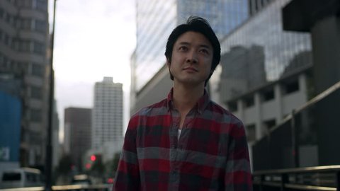 Casual Japanese man walking down a quiet city street and stops to answer his mobile phone with a look of concern with soft natural lighting. Medium shot on 4k RED camera.