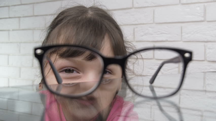 Peeking. A child with glasses. Little girl with pigtails is peeking under the table and wearing her eyeglasses