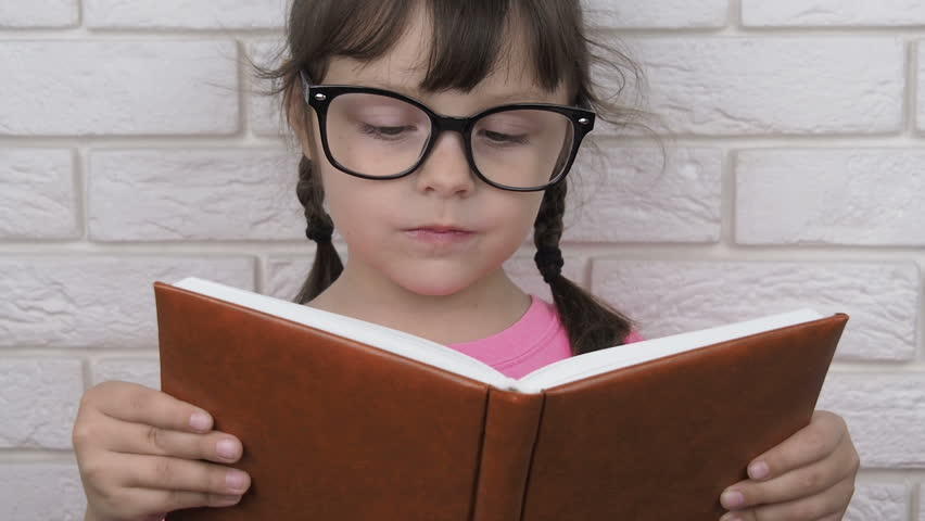 The child is reading a book. Closing book. Girl wearing glasses close her book that she was reading a moment ago.