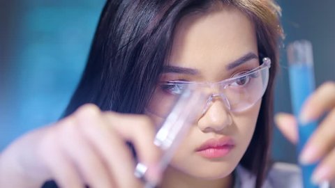 Close-up face of busy Asian female chemist mixing substances for molecular analysis