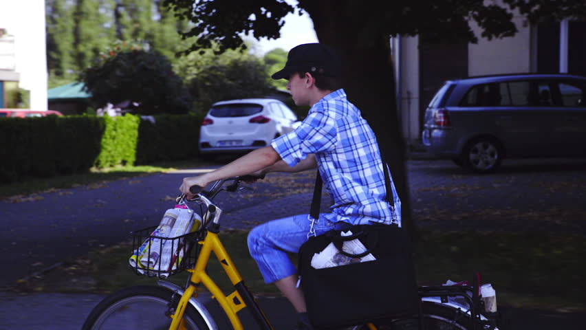 Boy with hat throwing newspaper while driving HD. Young boy postman driving yellow bicycle and delivering early morning newspaper, throwing far from street to house.