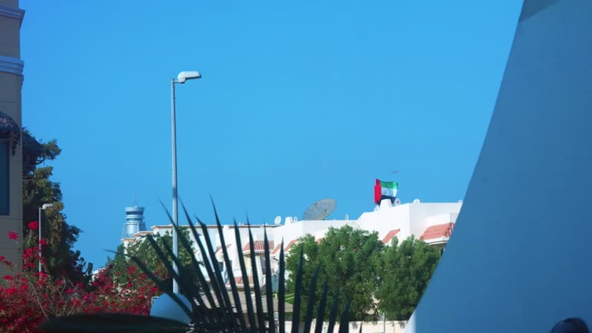 The United Arab Emirates flag waving above a house on an early clear morning with an airplane flying by