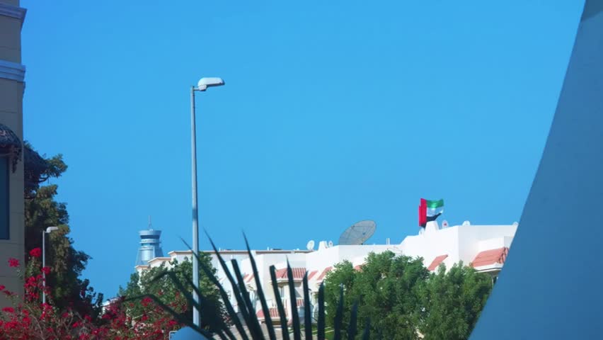 The United Arab Emirates flag waving above a house on an early clear morning with an airplane flying by