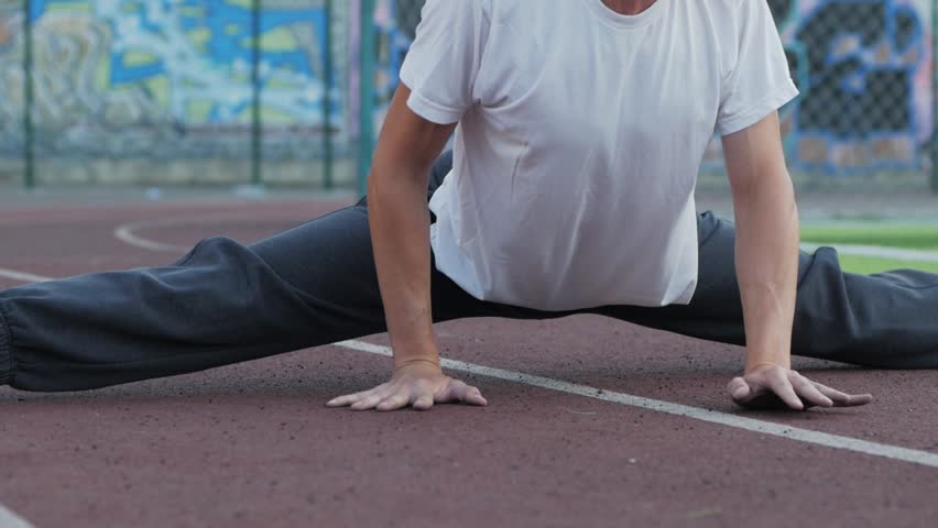 young male with unusual appearance do stretching exercises outdoors on sports ground, athlete makes workout.	