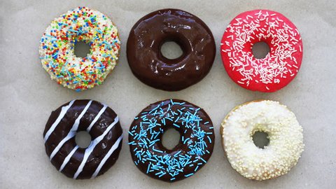 Donuts of different colors on cardboard, top view, stop motion animation. Full HD